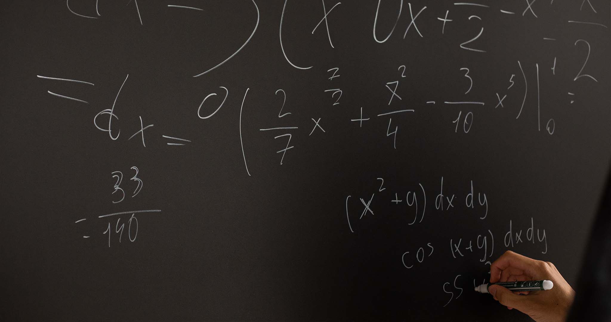 Une main écrit sur un tableau noir des mathématiques